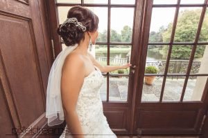 braut steht vor dem fenster im schloss dyck und schaut in den park mit dem teich