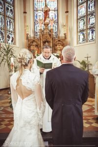 Hochzeitsfoto während Pastor Trauung der Braut und des Bräutigams vollzieht. Jesus Figur und Altar im Hintergrund am Altar der St. Antoniuskirche in Swisttal.