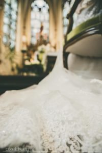 Hochzeitsfoto aus der Froschperspektive. Detailfoto des Brautkleides. Altar der St. Antonius Kirche in Swisttal in unscharfem Hintergrund zu sehen.