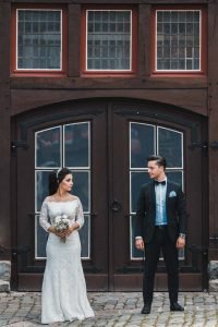 Brautpaar posiert vor einer Doppeltür mit drei Fenstern darüber, im Innenhof der Burg Altena. Sie schauen sich an, der Hochzeitsfotograf fotografiert sie frontal. Symetriesches Foto.