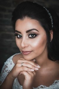 Eine schöne Pose der Braut. Sie faltet ihre Hände unter ihrem Kinn, an ihrer rechten Hand steckt ihr Verlobungsring. Das Makro-Ringlicht reflektiert in den Augen der Braut.