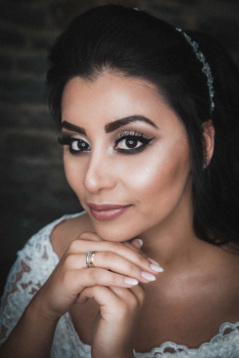 Eine schöne Pose der Braut. Sie faltet ihre Hände unter ihrem Kinn, an ihrer rechten Hand steckt ihr Verlobungsring. Das Makro-Ringlicht reflektiert in den Augen der Braut.