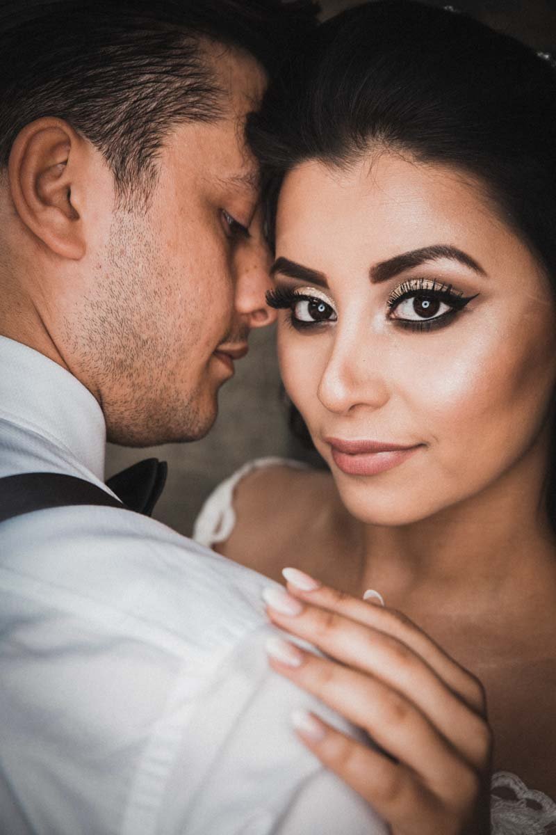 Eine schöne Pose der Braut an der Schulter des Bräutigam der mit dem Rücken zum Hochzeitsfotografen steht, Die Ringlichtbeleuchtung reflektiert in den Augen der Braut.
