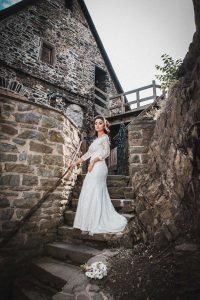 Braut schaut zum Hochzeitsfotografen, auf einer Treppe in der Burg Altena, ihr Brautstrauß liegt auf der Treppe