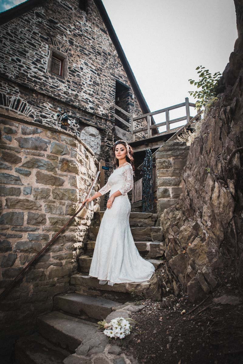 Braut schaut zum Hochzeitsfotografen, auf einer Treppe in der Burg Altena, ihr Brautstrauß liegt auf der Treppe