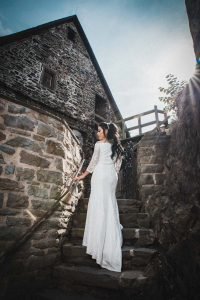 Braut steht mit dem Rücken zum Hochzeitsfotografen, auf einer Treppe in der Burg Altena, die Sonne scheint in obiger rechten Position