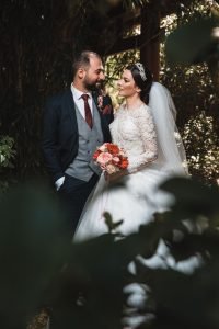 Hochzeitsfoto eines Brautpaares im japanischen Garten in Leverkusen. Hochzeitsfotograf steht hinter Ästen und beobachtet das Paar aus einer Voyeur-Perspektive. Kreatives Hochzeitsfoto.