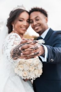 Hochzeitsfotograf Bruehl Schloesser - somalisch afrikanisch hochzeit - Hochzeitsreportage_2_Brautpaar Shooting Hände des Brautpaares sind ineinander verschränkt und zeigen Hennatatoo und Eheringe Brautstrauß unscharf im Hintergrund sichtbar